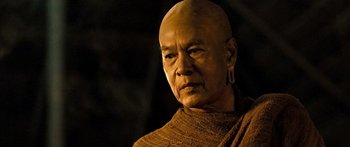 Movie still from “Ong Bak 3” (2010), directed by Tony Jaa – An older man with a bald head wearing a brown sweater; Close Up shot, Low angle