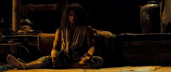 Movie still from “Ong Bak 3” (2010), directed by Tony Jaa – A man sitting on the ground in a dark room; Medium shot, Low angle