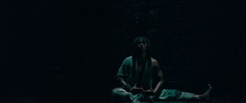 Movie still from “Ong Bak 3” (2010), directed by Tony Jaa – A man sitting on the ground in a dark room; Medium shot, Low angle