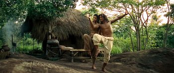 Movie still from “Ong Bak 3” (2010), directed by Tony Jaa – A man and a woman standing next to each other in front of a hut; Wide shot, Low angle