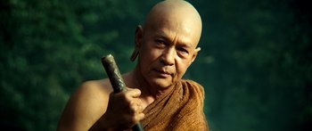 Movie still from “Ong Bak 3” (2010), directed by Tony Jaa – A bald man with a shaved head holding a stick; Close Up shot, Low angle