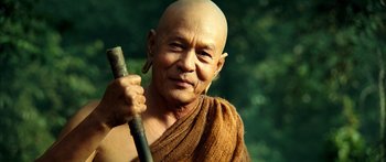 Movie still from “Ong Bak 3” (2010), directed by Tony Jaa – An older man with a shaved head holding a stick; Close Up shot, Low angle
