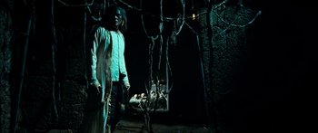 Movie still from “Ong Bak 3” (2010), directed by Tony Jaa – A man standing in a dark room next to a bunch of trees; Wide shot, Low angle