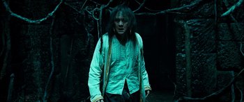 Movie still from “Ong Bak 3” (2010), directed by Tony Jaa – A man with long dreadlocks standing next to a tree; Medium shot, Low angle