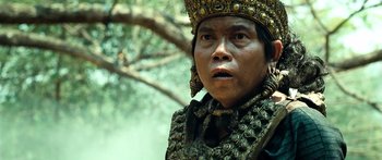 Movie still from “Ong Bak 3” (2010), directed by Tony Jaa – A man wearing a gold crown and a black and gold outfit; Close Up shot, Over the shoulder angle