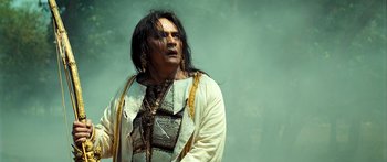 Movie still from “Ong Bak 3” (2010), directed by Tony Jaa – A man with long black hair wearing a white shirt; Medium shot, Low angle