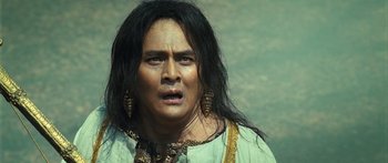 Movie still from “Ong Bak 3” (2010), directed by Tony Jaa – A man with long black hair wearing a green shirt; Close Up shot, Low angle