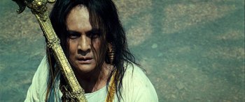 Movie still from “Ong Bak 3” (2010), directed by Tony Jaa – A man with long black hair wearing a white shirt and gold earrings; Close Up shot, Low angle