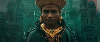 Movie still from “Ong Bak 3” (2010), directed by Tony Jaa – A man in a gold hat and a gold necklace; Close Up shot, Low angle