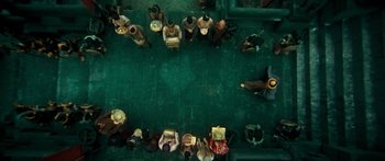 Movie still from “Ong Bak 3” (2010), directed by Tony Jaa – A group of people standing around each other on a green floor; Extreme Wide shot, Overhead angle