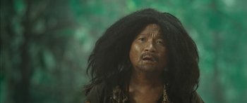 Movie still from “Ong Bak 3” (2010), directed by Tony Jaa – An asian man with long black hair looking at the camera; Close Up shot, Low angle