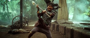 Movie still from “Ong Bak 3” (2010), directed by Tony Jaa – A man in costume holding a sword in a forest; Medium shot, Low angle