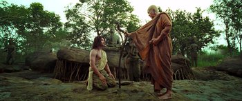 Movie still from “Ong Bak 3” (2010), directed by Tony Jaa – A man is kneeling on the ground while another man holds a stick; Wide shot, Low angle