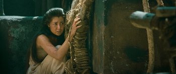 Movie still from “Ong Bak 3” (2010), directed by Tony Jaa – A woman leaning against a wall holding a rope; Medium shot, High angle