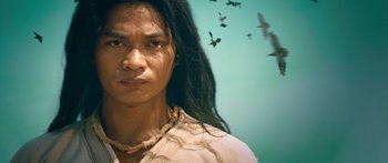 Movie still from “Ong Bak 3” (2010), directed by Tony Jaa – A man with long dreadlocks standing in front of a flock of birds; Close Up shot, Low angle