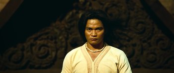 Movie still from “Ong Bak 3” (2010), directed by Tony Jaa – A man with long black hair wearing a yellow shirt; Close Up shot, Low angle