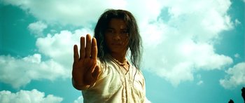 Movie still from “Ong Bak 3” (2010), directed by Tony Jaa – A man with long black hair is holding up his hand; Close Up shot, Low angle