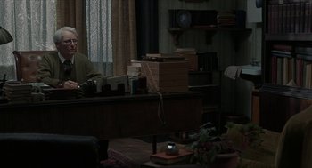 Movie still from “Suspiria” (2018), directed by Luca Guadagnino – An older man sitting at a desk in front of a laptop computer; Medium shot, Over the shoulder angle