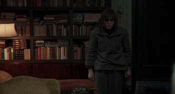Movie still from “Suspiria” (2018), directed by Luca Guadagnino – A woman standing in front of bookshelves in a room; Medium shot, Over the shoulder angle