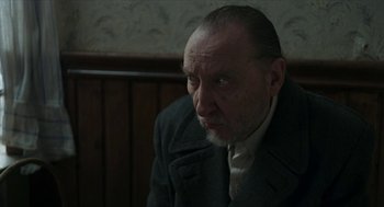 Movie still from “Suspiria” (2018), directed by Luca Guadagnino – An older man in a jacket and tie looking into the distance; Close Up shot, Over the shoulder angle