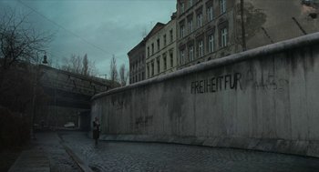 Movie still from “Suspiria” (2018), directed by Luca Guadagnino – A person standing on a sidewalk next to a wall; Wide shot, Low angle