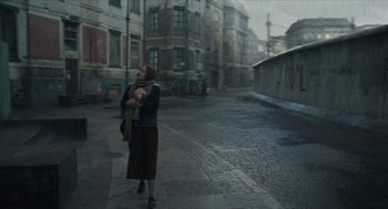 Movie still from “Suspiria” (2018), directed by Luca Guadagnino – A woman walking down the street holding a baby in her arms; Wide shot, Over the shoulder angle