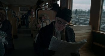 Movie still from “Suspiria” (2018), directed by Luca Guadagnino – An older man reading a newspaper while sitting on a train; Medium shot, Over the shoulder angle