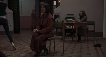 Movie still from “Suspiria” (2018), directed by Luca Guadagnino – A woman sitting on a chair in front of a camera; Wide shot, High angle