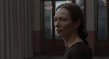 Movie still from “Suspiria” (2018), directed by Luca Guadagnino – A woman is looking into the distance in a dark room; Close Up shot, Over the shoulder angle