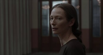 Movie still from “Suspiria” (2018), directed by Luca Guadagnino – A woman with long dark hair wearing a black shirt; Close Up shot, Over the shoulder angle