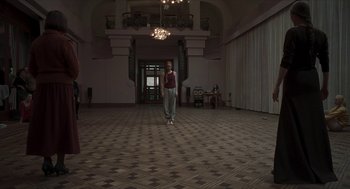 Movie still from “Suspiria” (2018), directed by Luca Guadagnino – A person standing in a room with a chandelier; Extreme Wide shot, Low angle