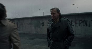 Movie still from “Suspiria” (2018), directed by Luca Guadagnino – A man in a trench coat standing in front of a wall; Medium shot, Over the shoulder angle