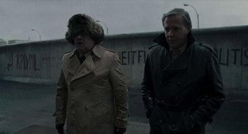 Movie still from “Suspiria” (2018), directed by Luca Guadagnino – Two men in coats and hats walking down a street; Medium shot, Over the shoulder angle