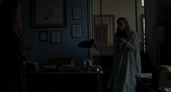 Movie still from “Suspiria” (2018), directed by Luca Guadagnino – A woman standing next to a desk in a dark room; Medium shot, Over the shoulder angle