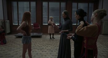 Movie still from “Suspiria” (2018), directed by Luca Guadagnino – A group of people standing in a room; Wide shot, Over the shoulder angle