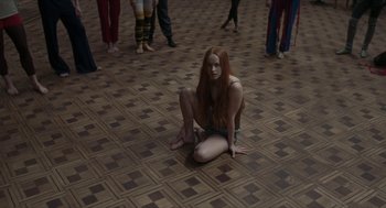 Movie still from “Suspiria” (2018), directed by Luca Guadagnino – A woman sitting on the ground in a room with people; Wide shot, High angle