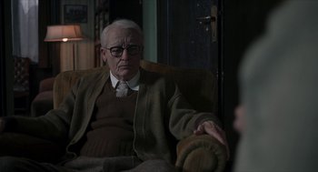 Movie still from “Suspiria” (2018), directed by Luca Guadagnino – An older man sitting in a chair in front of a door; Medium shot, Over the shoulder angle