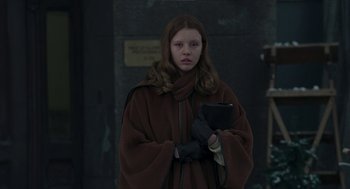 Movie still from “Suspiria” (2018), directed by Luca Guadagnino – A woman in a brown coat holding a cup in her hand; Medium shot, Over the shoulder angle