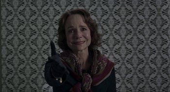 Movie still from “Suspiria” (2018), directed by Luca Guadagnino – An older woman wearing gloves and a scarf points at the camera; Close Up shot, Over the shoulder angle