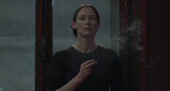 Movie still from “Suspiria” (2018), directed by Luca Guadagnino – A woman smoking a cigarette in front of a window; Close Up shot, Over the shoulder angle