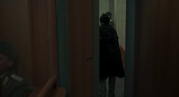 Movie still from “Suspiria” (2018), directed by Luca Guadagnino – A man is walking through a bathroom door way; Medium shot, Over the shoulder angle