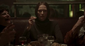 Movie still from “Suspiria” (2018), directed by Luca Guadagnino – A woman sitting at a table smoking a cigarette; Medium shot, Over the shoulder angle