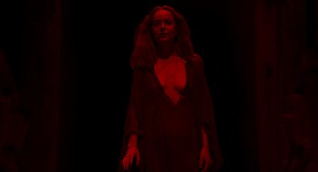 Movie still from “Suspiria” (2018), directed by Luca Guadagnino – A woman standing in the dark wearing a red dress; Medium shot, Overhead angle