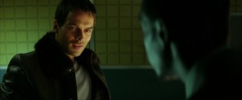 Movie still from “Swordfish” (2001), directed by Dominic Sena – A man standing in front of another man in a dark room; Close Up shot, Over the shoulder angle