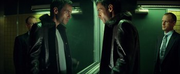 Movie still from “Swordfish” (2001), directed by Dominic Sena – Two men looking at each other in a dark room; Medium shot, Over the shoulder angle