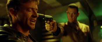 Movie still from “Swordfish” (2001), directed by Dominic Sena – A man holding a gun pointed at another man; Close Up shot, Over the shoulder angle