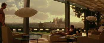 Movie still from “Swordfish” (2001), directed by Dominic Sena – A woman sitting on a lounge chair in front of a city skyline; Extreme Wide shot, Low angle