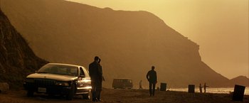 Movie still from “Swordfish” (2001), directed by Dominic Sena – Two men standing on a beach near some cars; Extreme Wide shot, Low angle