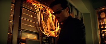 Movie still from “Swordfish” (2001), directed by Dominic Sena – A man in a black shirt is looking at a bunch of wires in front of him; Close Up shot, Low angle