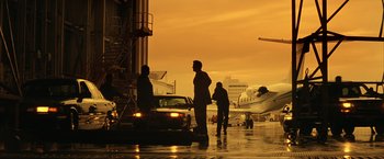 Movie still from “Swordfish” (2001), directed by Dominic Sena – A man standing next to a car in front of an airplane; Extreme Wide shot, Low angle